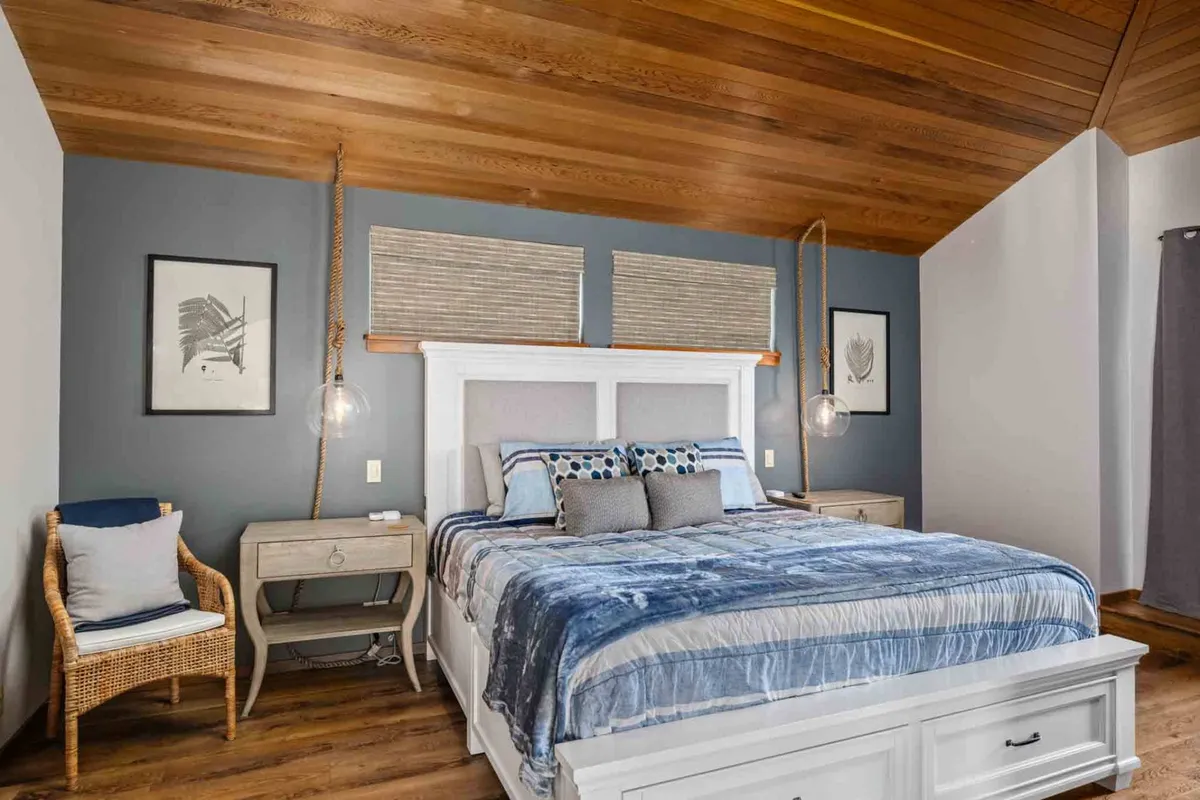 This serene bedroom features a plush bed adorned with decorative pillows, a cozy wicker chair, and tasteful artwork on the walls. Soft natural light filters in, creating a peaceful and restful atmosphere.