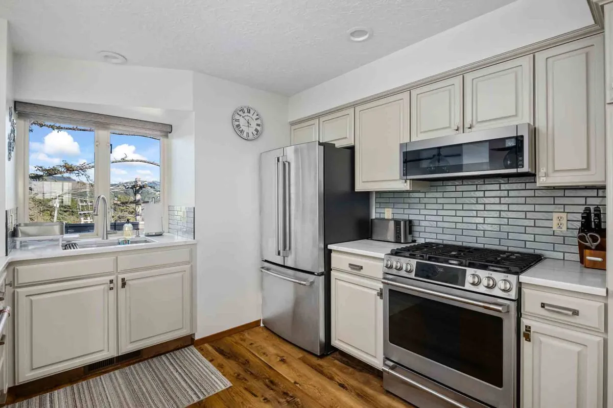 A bright kitchen space with white cabinetry, stainless steel appliances, and a modern backsplash, all bathed in natural light from a window offering a view. The layout hints at ample space for cooking and hosting.