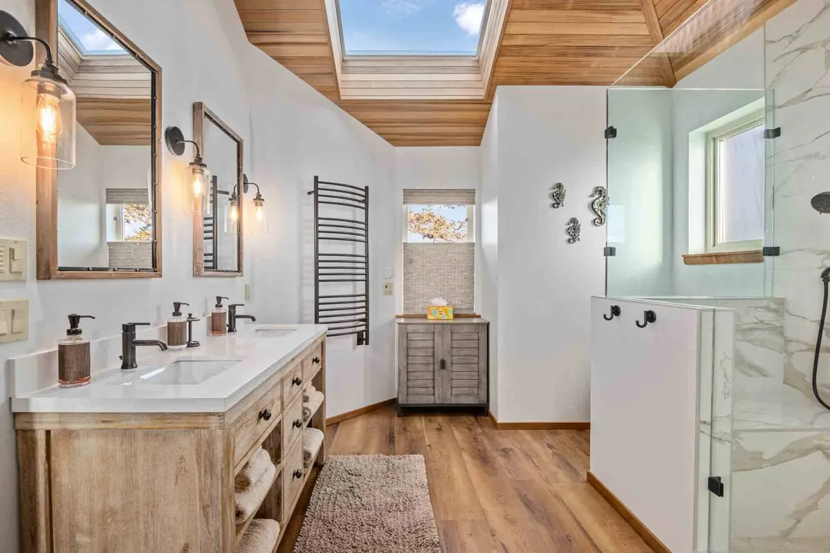 A modern, spa-inspired bathroom featuring a double sink vanity, a skylight that brings in abundant natural light, a walk-in shower, and elegant wooden accents. The overall mood is calming and rejuvenating.