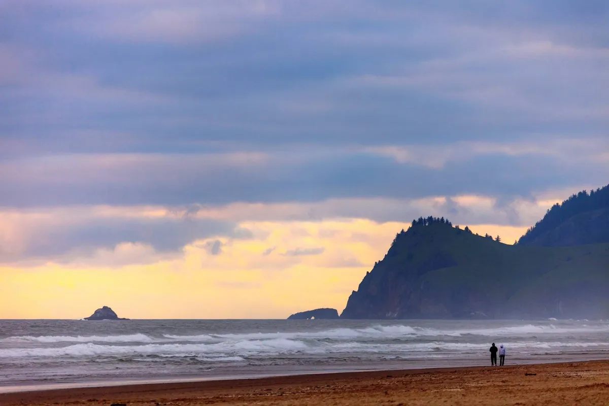 A picturesque shot of ocean waves and distant cliffs, with a couple walking along the beach. The setting is romantic and tranquil, evoking the coastal charm of Lincoln City and the proximity to oceanfront attractions.