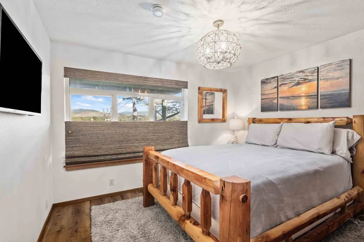 An inviting bedroom with a striking log bed, warm landscape artwork, a modern light fixture, and a window that floods the space with natural light. The setting feels both relaxing and distinctively styled.