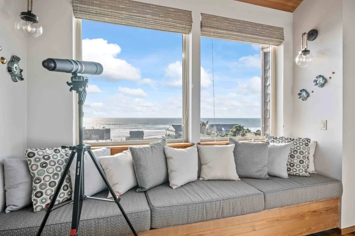 A tranquil seating nook with a telescope set beside wide picture windows that frame dramatic ocean views. Soft furnishings and decorative pillows add a touch of understated luxury, while the telescope hints at activities like whale watching and stargazing.