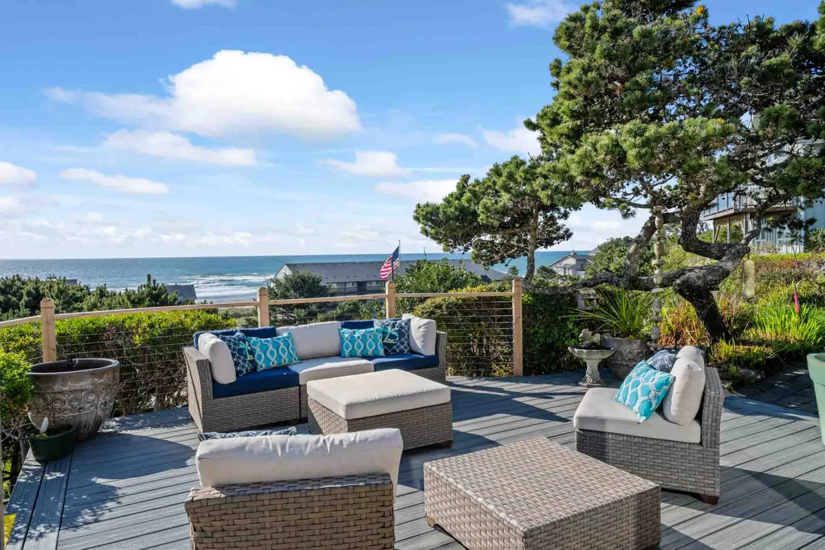 This image showcases an inviting outdoor seating area set against a breathtaking ocean view. Decorative cushions and lush greenery add warmth and comfort, perfectly illustrating a space ideal for relaxing, socializing, or simply soaking in the natural surroundings.