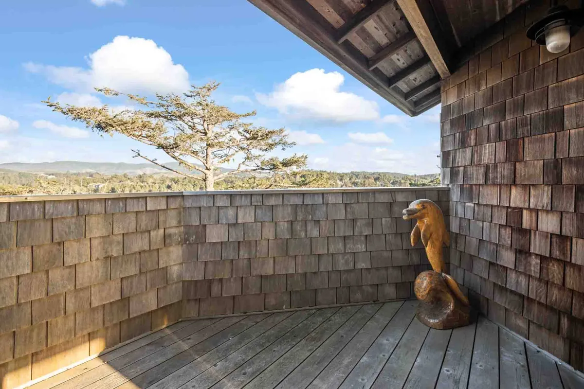 An exterior shot of a private wooden deck adorned with a carved otter sculpture and surrounded by greenery. The deck provides a serene space for relaxation, meditation, or enjoying the scenic natural surroundings.