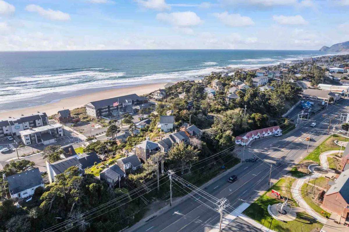 A wide-angle view featuring ocean waves, the sandy beach, a coastal road, and the nearby town center. The image evokes a sense of adventure and easy access to both natural and community amenities.